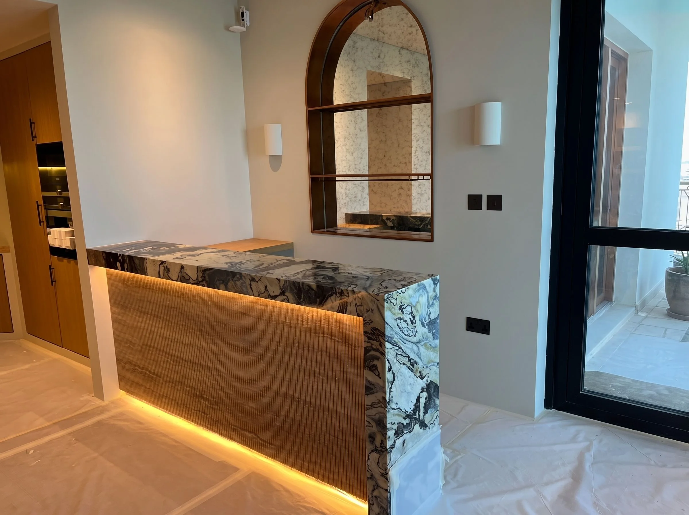 Bar counter in a Dubai Marina apartment: a veined stone top that wraps down the end, over a fluted, backlit front.