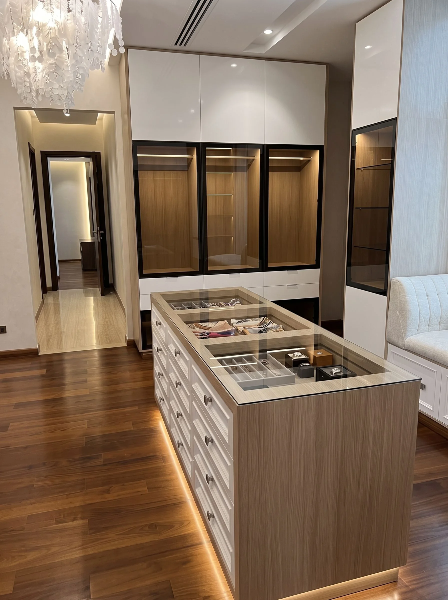 Dressing room in an Umm Suqeim villa: a glass-topped island of drawers between lit wardrobes.